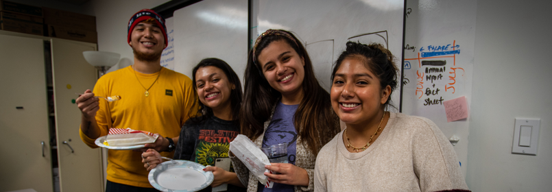 four students holding plates of food smile at the camera 