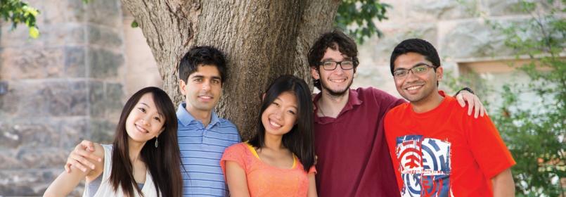 Five smiling students gathered near a tree